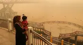 Seorang ibu bersama anaknya yang mengenakan masker melihat kondisi sekitar dari atas jembatan di tengah kabut asap tebal akibat kebakaran hutan dan lahan di Palangkaraya, Kalimantan Tengah, Senin (12/10/2026). Kabut asap menyelimuti sejumlah wilayah di Indonesia, Malaysia, dan Singapura selama beberapa pekan terakhir akibat kebakaran yang melanda kawasan hutan di Kalimantan dan Sumatra. Asap dari kebakaran tersebut terbawa angin hingga melintasi wilayah regional dan berdampak pada kualitas udara. (Reina/AFP)