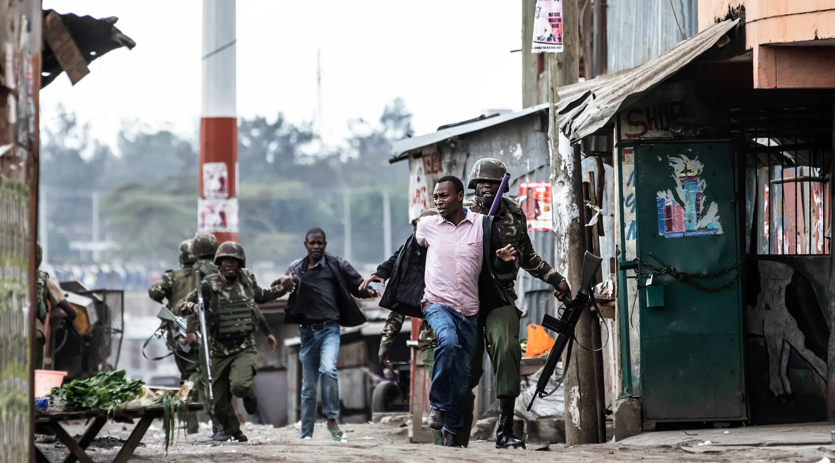 Petugas keamanan Kenya membawa seorang pria usai terjadi pembunuhan saat kericuhan perkampungan Mathare di Nairobi, Kenya (9/8). (AFP Photo/Marco Longari)