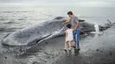Warga mengajak anaknya melihat bangkai paus sperma yang terdampar, sementara petugas konservasi masih menyelidiki penyebab kematiannya, menjelang rencana penguburan di salah satu tempat di pantai Banjar Anyar Sari, Desa Nusasari, Kecamatan Melaya, Jembrana, Bali, pada Rabu 6 Mei 2026. Seekor ikan paus sperma dengan panjang sekitar lima belas meter terdampar dalam keadaan mati. (Lana Priatna/AFP)