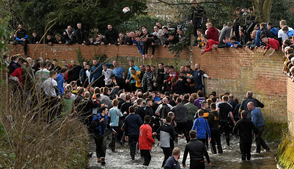 Para peserta menyusuri sungai untuk berebut bola saat mengikuti Royal Shrovetide Football Match di Ashbourne, Derbyshire, Inggris, Selasa (5/3). Pertandingan ini menghalalkan segala macam cara untuk menang. (Oli Scarff/AFP)