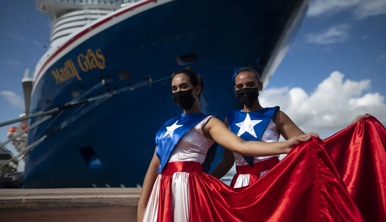 Ivanelis Jimenez (depan) dan Veronica Barreto mengenakan gaun bendera Puerto Rico saat menyambut penumpang kapal pesiar Mardi Gras Carnival yang berlabuh di Teluk San Juan, Puerto Rico, Selasa (3/8/2021). (AP Photo/Carlos Giusti)