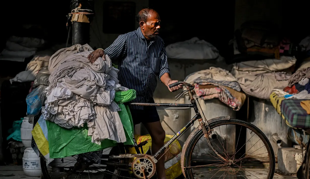 Seorang pekerja mengumpulkan pakaian yang sudah dicuci untuk dikeringkan di binatu terbuka, yang secara lokal disebut 'Dhobi Ghat' di New Delhi, India pada 14 Maret 2022. Dhobi Ghat adalah tempat yang menyediakan layanan cuci dengan cara tradisional. (Money SHARMA / AFP)