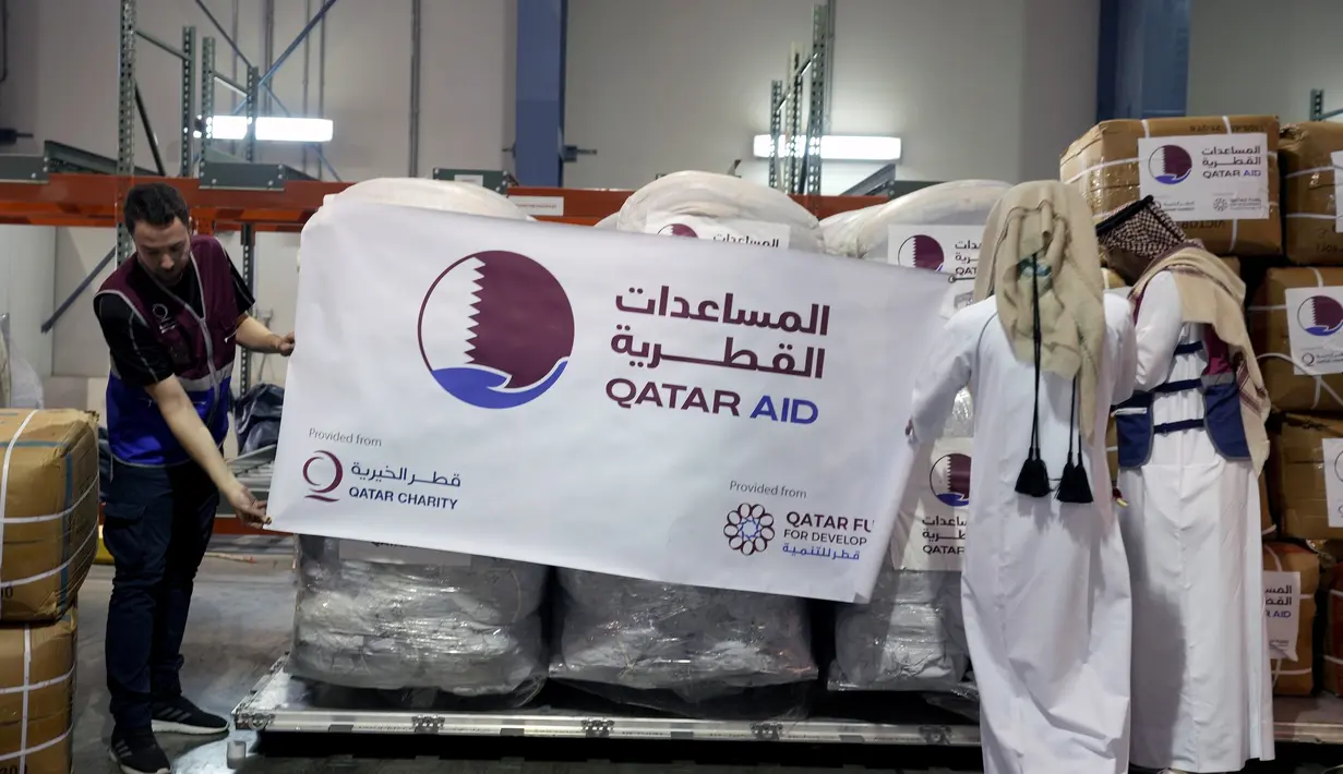Karyawan Bulan Sabit Merah Qatar memegang spanduk berisi paket bantuan yang akan dikirim untuk wilayah yang terkena gempa di Turki, di Pangkalan Udara Al-Udeid di Qatar, Selasa, 7 Februari 2023. Gempa bumi dahsyat melanda Turki tenggara dan Suriah Senin dini hari, merobohkan ratusan bangunan serta menewaskan dan melukai ribuan orang. (AP Photo/Kamran Jebreili)