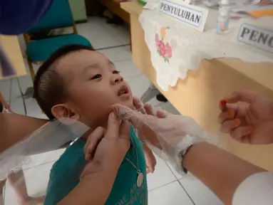Bidan dibantu Kader Posyandu memberikan vaksin vitamin A dan imunisasi di Posyandu RW 20, Kelurahan Pondok Benda, Tangerang Selatan, Selasa (18/8/2020). Pemerintah sudah mengaktifkan pelayanan posyandu ketiga sejak pandemi Covid-19 dengan memperketat protokol kesehatan. (merdeka.com/Dwi Narwoko)