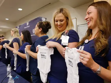 Paige Packard dan Allison Thompson memegang pakaian bayi ketika konferensi pers bersama 16 suster di bagian gawat darurat sebuah rumah sakit di Mesa, Arizona yang sedang hamil pada periode yang relatif bersamaan, 17 Agustus 2018. (AP/Ross D. Franklin)