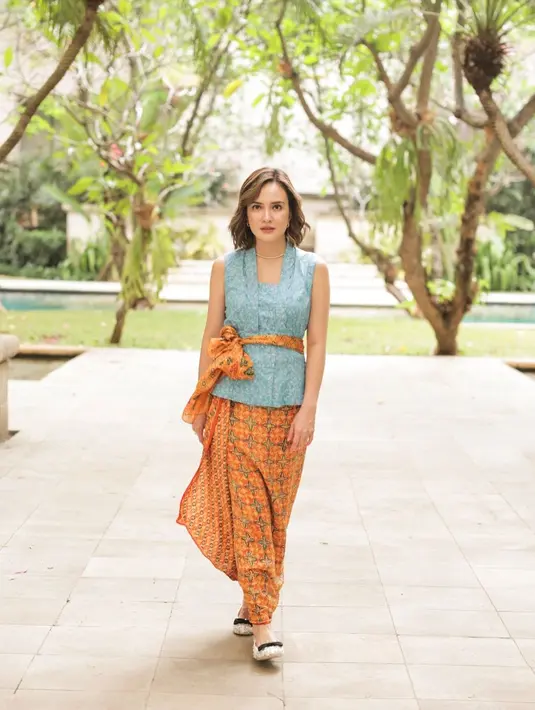 Tampilan stylish Shandy Aulia kenakan kebaya bali model tanpa lengan. Kebaya warna biru muda itu berpadu sempurna dengan kain dan selendang oranye.[@shandyaulia].