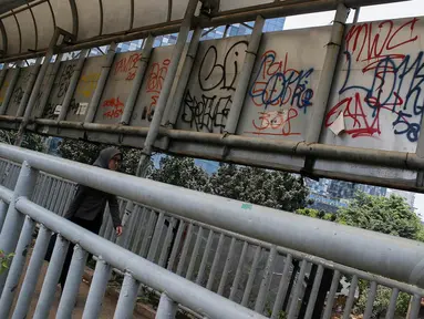 Pejalan kaki melewati vandalisme yang dilakukan orang tak bertanggung jawab di JPO depan Mall Kasablanka, Jakarta, (18/9/14). (Liputan6.com/Faizal Fanani)