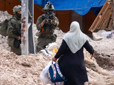 Seorang tentara Israel mengangkat senapannya saat warga Palestina membawa barang-barang mereka setelah diperintahkan untuk meninggalkan rumah mereka selama operasi Israel di kamp pengungsi Tulkarem di barat laut Tepi Barat yang diduduki pada 2 Mei 2025. (Jaafar ASHTIYEH/AFP)