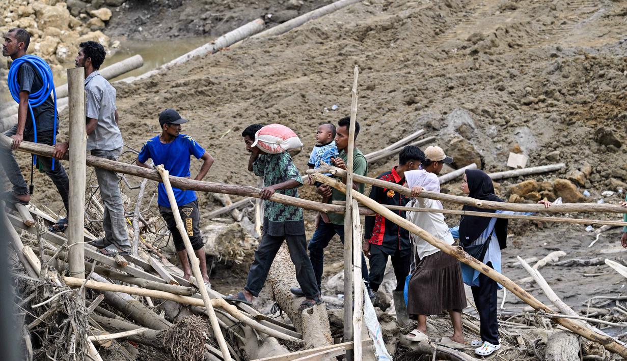 Struktur jembatan baja tersebut ditargetkan menjadi penghubung sementara agar mobilitas masyarakat dan distribusi logistik ke wilayah terdampak dapat kembali berjalan. Tampak dalam foto, warga menyeberangi sungai di jembatan yang baru dibangun yang menghubungkan Aceh dan Provinsi Sumatera Utara setelah hancur akibat banjir bandang di Sungai Peusangan, Distrik Bireuen, Provinsi Aceh, Selasa 9 Desember 2025. (CHAIDEER MAHYUDDIN/AFP)