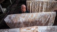 Seorang wanita mewarnai kain batik saat proses pembuatan di Sidoarjo, Jawa Timur, Sabtu (1/10/2022). Indonesia akan memperingati Hari Batik Nasional pada 2 Oktober. (JUNI KRISWANTO/AFP)