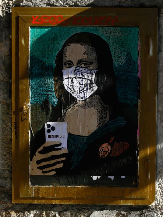 Poster seniman Italia TVBOY yang menggambarkan Mona Lisa karya Leonardo da Vinci mengenakan masker dan memegang smartphone di jalan Barcelona, Selasa (18/2/2020). Instalasi muncul setelah Mobile World Congress (MWC) 2020 batal digelar lantaran wabah virus corona yang mencekam. (PAU BARRENA/AFP)