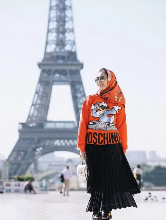 Berada di Paris, Dine tampil dengan sweater Moschino merah serasi dengan kerudung motif kupu-kupunga. Dipadukan rok plisket bertumpuk hitam. Credit: Instagram @dine.pearl