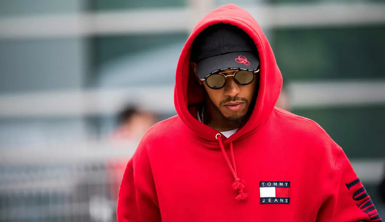Pembalap Mercedes asal Inggris Lewis Hamilton berjalan di paddock sebelum Grand Prix Formula Satu China di Shanghai (12/4). Hamilton keren mengenakan kaca mata dan jaket berwarna merah. (AFP Photo/Johannes Eisele)