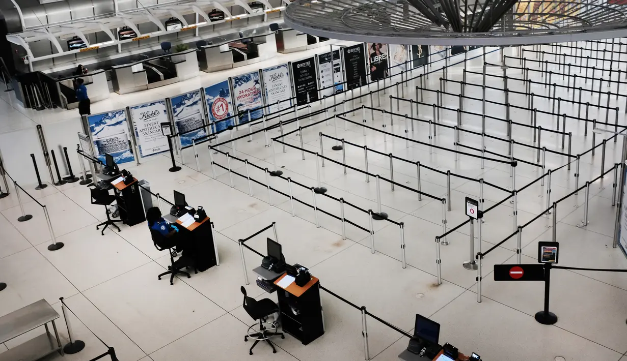 Orang-orang berjalan melalui terminal keberangkatan internasional yang sepi di Bandara John F. Kennedy (JFK), New York City, Sabtu (8/3/2020). Maskapai penerbangan terpukul wabah virus corona (COVID-19) setelah pelancong bisnis maupun rekreasi membatalkan rencana. (Spencer Platt/Getty Images/AFP)