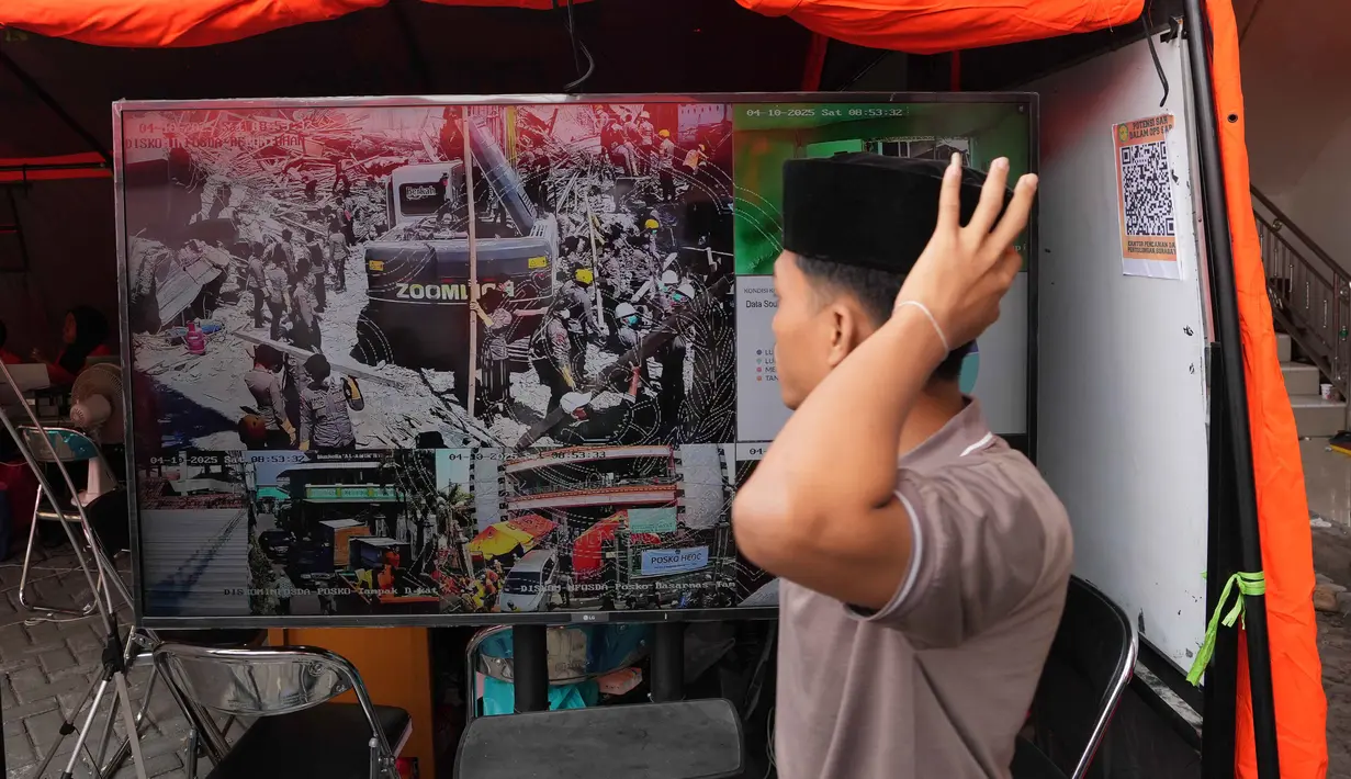 Seorang santri berjalan melewati layar TV yang menayangkan upaya pencarian korban hilang dari reruntuhan bangunan di sebuah pondok pesantren di Sidoarjo, Jawa Timur, Sabtu 4 Oktober 2025. (AP Photo/Achmad Ibrahim)