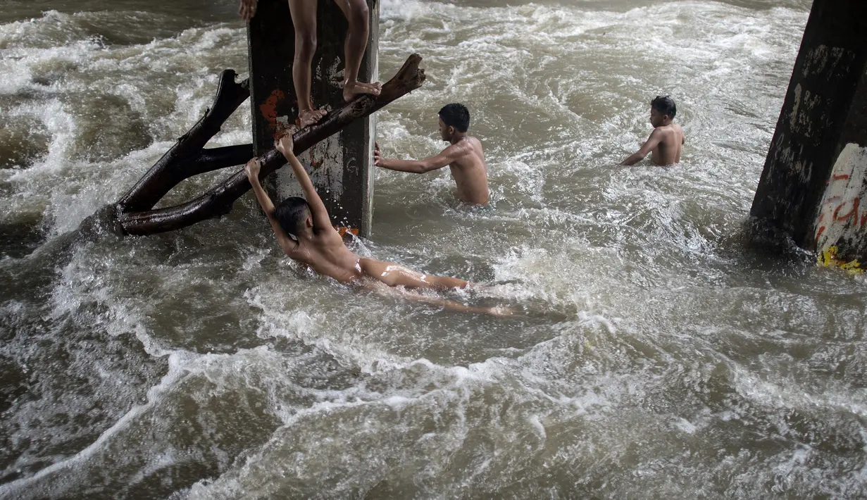 Sejumlah anak bermain di sungai dengan arus yang sangat deras akibat hujan lebat di bawah jembatan di Manila, Filipina (11/6). (AFP Photo/Noel Celis)