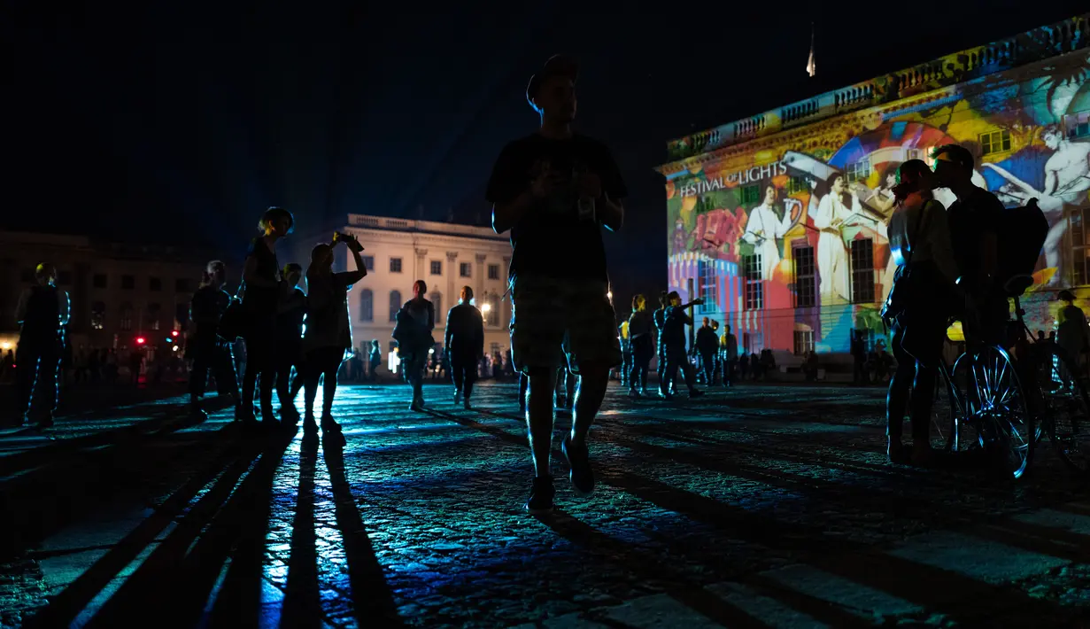 Sepasang kekasih berpelukan di depan Berlin State Opera (Staatsoper) yang diterangi cahaya dalam Festival of Lights di Berlin pada 14 September 2020. Kreasi cahaya lebih dari 90 karya seni tersebut ditampilkan di 86 lokasi yang berlangsung hingga 20 September mendatang. (John MACDOUGALL/AFP)