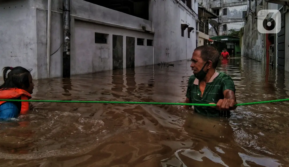 Warga berpegangan pada tali saat berjalan menyusuri banjir yang merendam permukiman di kawasan Kebalen, Jakarta, Sabtu (20/2/2021). Curah hujan yang tinggi menyebabkan banjir setinggi orang dewasa di kawasan Kebalen. (Liputan6.com/Johan Tallo)