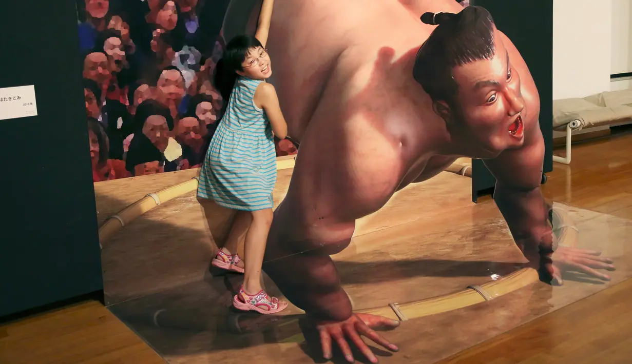 Seorang gadis berpose dengan gambar 3D pesumo pada pameran seni trik 3D karya seniman Jepang Masashi Hattori di Kawasaki, dekat Tokyo, Sabtu, (5/8). (AP Photo / Koji Sasahara)