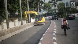 Pejalan kaki melintas saat pekerja dibantu alat berat merevitalisasi trotoar di kawasan Bundaran HI, Jakarta Pusat, Senin (15/7/2019). Penantaan ini dilakukan untuk mempercantik trotoar dan memberikan rasa nyaman bagi pejalan kaki. (Liputan6.com/Faizal Fanani)