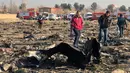 Orang-orang berjalan di antara puing-puing setelah pesawat Boeing 737 jatuh di dekat Bandara Internasional, Teheran, Iran, Rabu (8/1/2020). Seluruh penumpang pesawat maskapai Ukraina yang membawa 176 orang termasuk kru tersebut dilaporkan tewas. (AFP Photo)