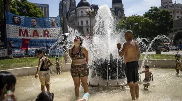 Orang-orang mendinginkan diri di air mancur, denggan latar belakang protes yang diselenggarakan oleh berbagai organisasi sosial berlangsung, di Buenos Aires, Argentina, Jumat (3/3/2023). Menurut Badan Meteorologi Nasional, Buenos Aires tetap dalam status siaga merah untuk suhu ekstrem. (AP Photo/Rodrigo Abd)