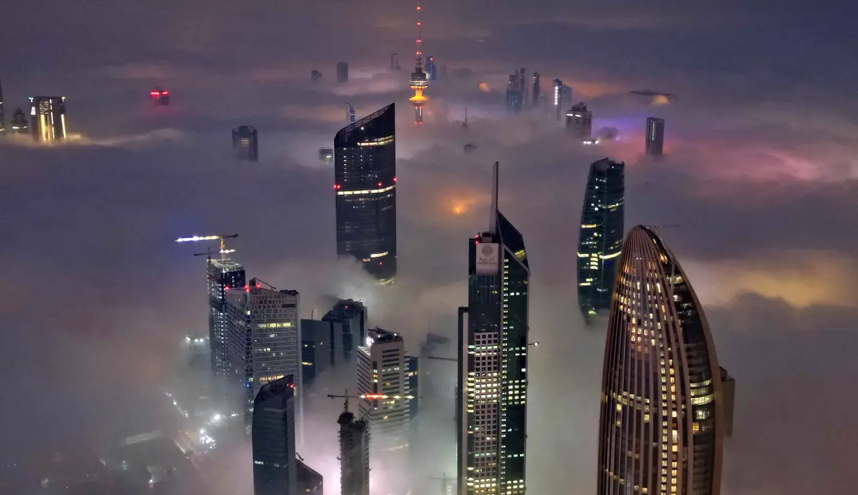 Suhu dingin dan kelembapan tinggi selama malam dan dini hari menciptakan kondisi ideal untuk terbentuknya kabut. Tampak foto udara memperlihatkan gedung pencakar langit yang tertutup kabut pagi di Kota Kuwait pada Minggu 9 November 2025. (YASSER AL-ZAYYAT/AFP)