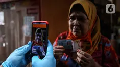 Warga penerima bantuan difoto petugas saat penyaluran Bantuan Sosial Tunai (BST) di RW 05 Kelurahan Kenari, Senen, Jakarta, Rabu (6/1/2021). Pencairan BST senilai Rp 300 ribu dilakukan dengan tiga cara, salah satunya diantar langsung ke rumah secara door to door. (Liputan6.com/Johan Tallo)