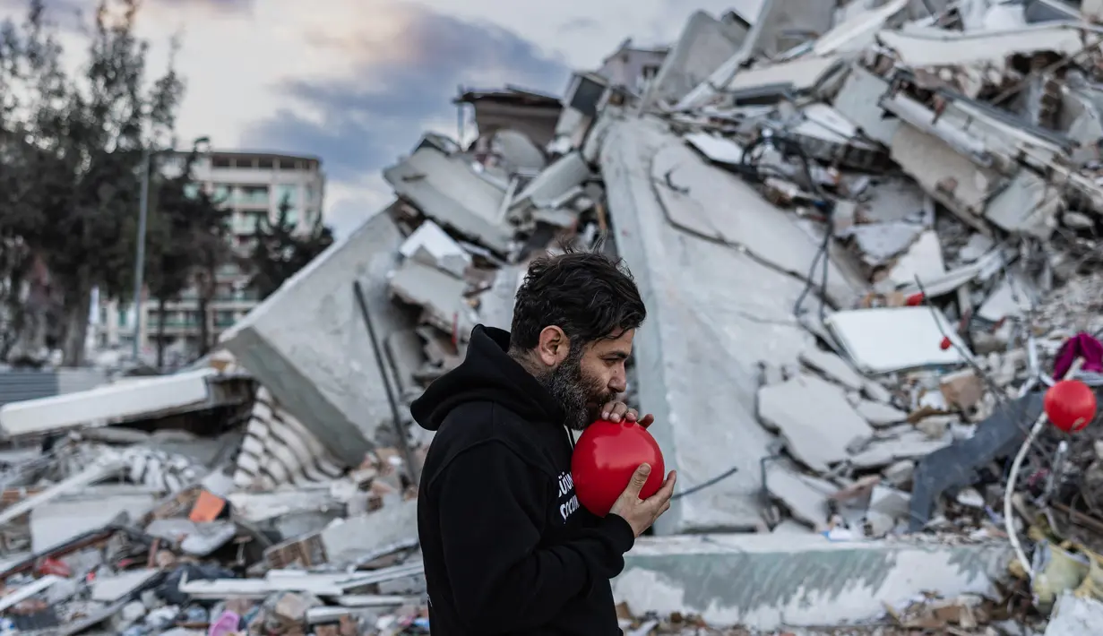 Ogun Sever Okur, pria Turki berusia 38 tahun menggembungkan balon di atas puing-puing bangunan yang runtuh di Antakya, Turki selatan pada 21 Februari 2023, menyusul gempa berkekuatan 6,4 yang melanda pada 20 Februari, dua minggu setelah gempa berkekuatan 7,8. gempa melanda dekat Gaziantep dan telah menewaskan lebih dari 44.000 orang. Di sisi jalan yang sibuk di Antakya, puluhan balon merah berkibar, bergelantungan di reruntuhan.  (AFP/Sameer Al-Doumy)