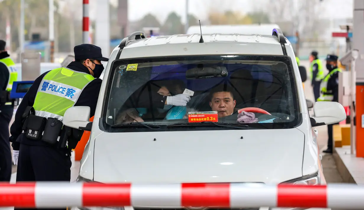 Polisi menggunakan termometer digital untuk mengukur suhu pengemudi mobil di sebuah pos pemeriksaan gerbang tol di Wuhan, Provinsi Hubei, China, Kamis (23/1/2020). Pemerintah China mengisolasi Kota Wuhan yang berpenduduk sekitar 11 juta jiwa untuk menahan penyebaran virus corona. (Chinatopix via AP)