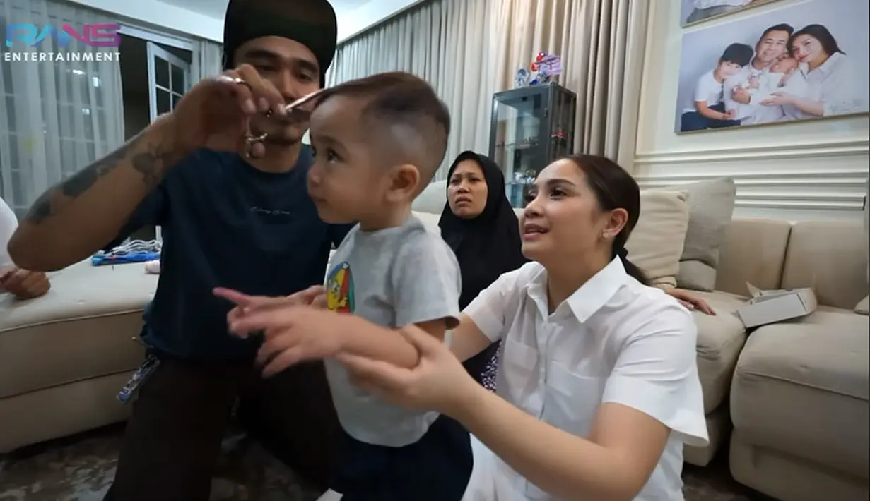 Seorang pria membantu merapikan rambut Cipung setelah Nagita memotong banyak yang tidak rata. Banyak netizen yang makin gemas dengan Cipung  setelah potong rambut. "Ngakak liat cipung jadi korban mama gigi jadi inget dulu waktu rambut aa rafathar juga jadi korban nya mama gigi wkwk," tulis Yussi Cheese.  [Youtube/Rans Entertainment]