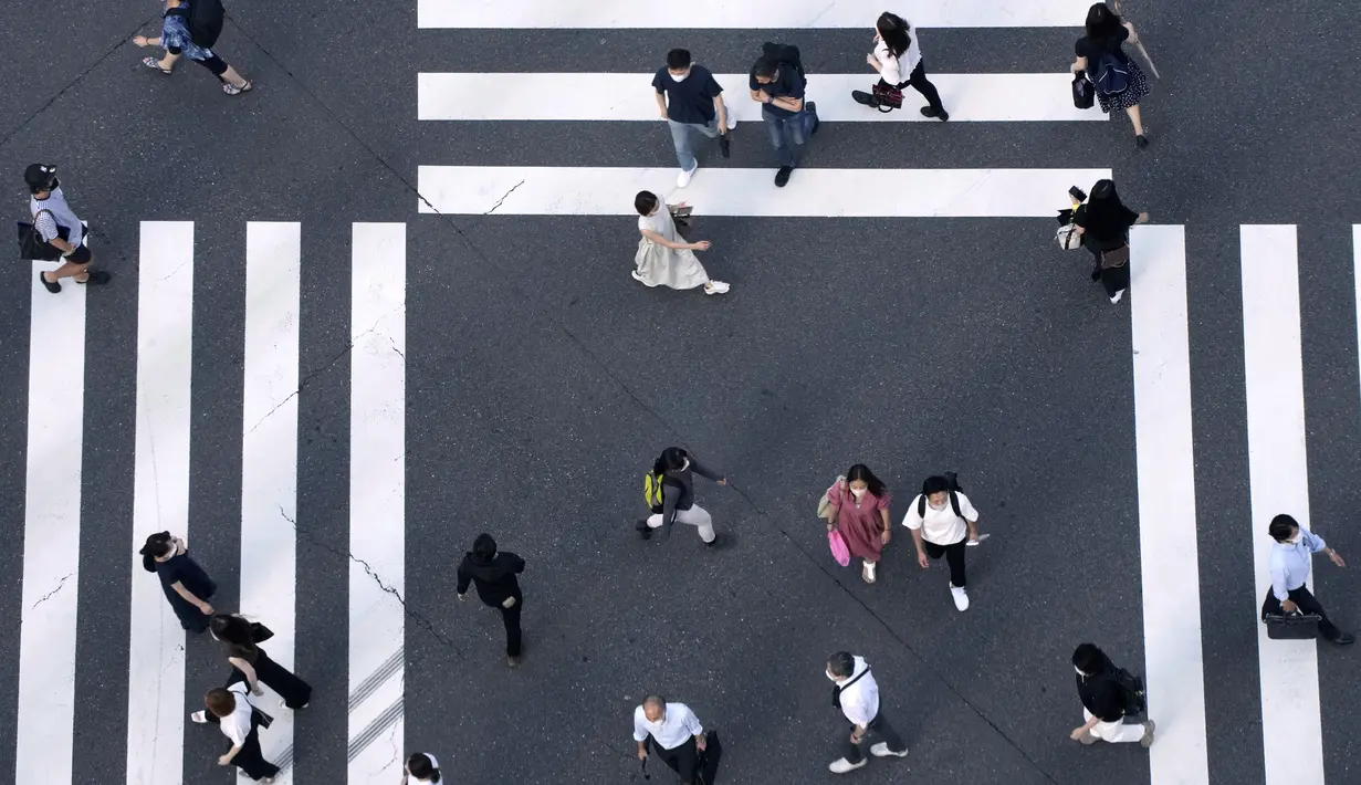 Warga yang mengenakan masker untuk membantu mengekang penyebaran COVID-19 berjalan di sepanjang penyeberangan pejalan kaki di Tokyo, Jepang, Selasa (27/7/2021). Tokyo melaporkan jumlah kasus harian COVID-19 tertinggi beberapa hari setelah Olimpiade dimulai. (AP Photo/Eugene Hoshiko)