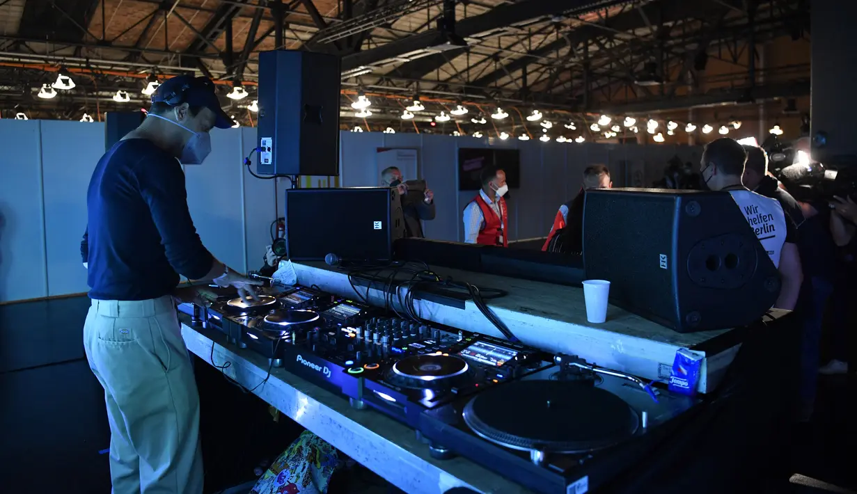 Seorang DJ tampil saat orang-orang tiba untuk menerima vaksinasi virus corona COVID-19 di pusat vaksinasi Arena Treptow, Berlin, Jerman, Senin (9/8/2021). Vaksinasi dengan diiringi musik DJ tersebut berlangsung pada malam yang panjang di tengah pandemi COVID-19. (John MACDOUGALL/POOL/AFP)