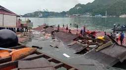 Orang-orang berdiri pada atap toko yang runtuh di pelabuhan setelah gempa magnitudo 5,1 di Jayapura, Provinsi Papua, Indonesia, 9 Februari 2023. Korban meninggal dalam gempa Jayapura adalah Rista (25), Ani (26), Astrid (25), dan Maya (27). (FAISAL NARWAWAN/AFP)