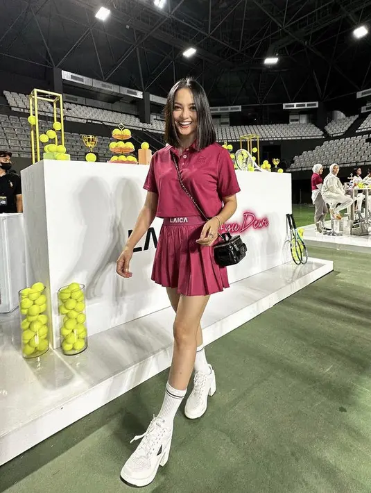 Ririn Ekawati tampil mengenakan pakaian warna sangria. Dengan atasan crop polo dipadu pleted skirt, dan sneakers heels putih. (@ririnekawati)