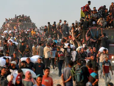 Orang-orang naik ke atas dan bergelantungan di atas truk yang mengangkut mereka, sementara yang lain berjalan sambil membawa karung-karung tepung di sepanjang jalan al-Rashid di Jabalia Barat pada 17 Juni 2025. (BASHAR TALEB/AFP)