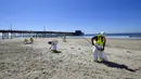 Pekerja membersihkan minyak dari pasir di Pantai Newport, California, Amerika Serikat, Selasa (5/10/2021). Kebocoran pipa menyebabkan tumpahan minyak di lepas pantai California. (Jeff Gritchen/The Orange County Register via AP)
