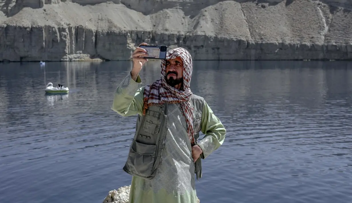 Seorang pria mengambil video dengan ponselnya di sebelah Danau Band e-Amir, Provinsi Bamiyan, 4 Oktober 2021. Danau Band-e Amir yang memiliki perairan biru menakjubkan disebut juga sebagai Grand Canyon Afghanistan. (BULENT KILIC/AFP)