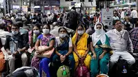 Orang India yang menunggu di stasiun kereta api memakai masker pelindung sebagai tindakan pencegahan terhadap pandemi Virus Corona. (Rajanish Kakade / AP Photo]