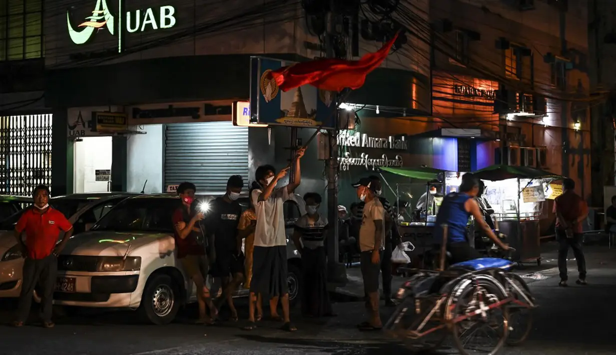 Orang-orang mengibarkan bendera partai Liga Nasional untuk Demokrasi (NLD) dan menyalakan ponsel mereka setelah seruan untuk protes keluar di media sosial di Yangon, Myanmar, 3 Februari 2021. Kudeta militer Myanmar terus memicu protes warga. (STR/AFP)