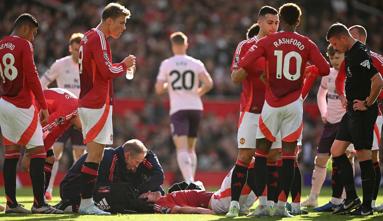 Pemain Manchester United, Matthijs de Ligt mendapatkan perawatan dari tim medis saat kepalanya mengalami pendarahan setelah berbenturan dengan pemain Brentford, Kevin Schade dalam laga lanjutan Liga Inggris 2024/2025 di Old Trafford, Manchester, Sabtu (19/10/2024). (AFP/Oli Scarff)