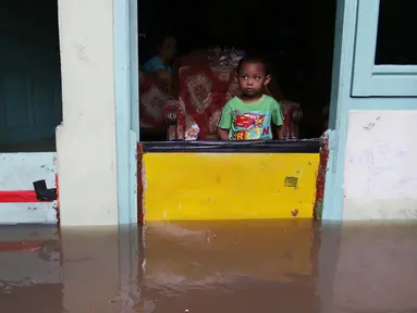 Seorang anak di dalam rumah memperhatikan banjir di kawasan Jatayu, Jakarta, Senin (21/11). Karena tingginya curah hujan serta buruknya drainase air menyebabkan meluapnya Kali Pesanggrahan yang mengakibatkan banjir. (Liputan6.com/Gempur M. Surya)