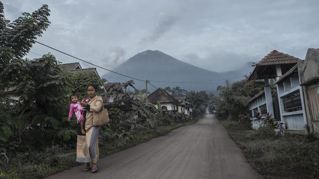<span>Gunung Semeru menjulang di atas desa Lumajang, Jawa Timur, setelah meletus sehari sebelumnya, Minggu (17/1/2021). Gunung Semeru kembali erupsi dan mengeluarkan awan panas guguran sejauh 4,5 kilometer pada Sabtu (16/1). (Juni Kriswanto / AFP)</span>