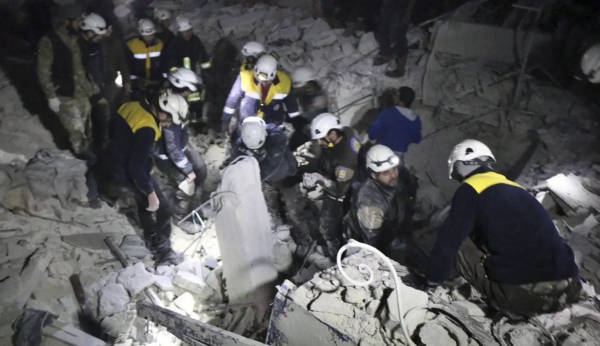 Relawan White Helmets membongkar reruntuhan bangunan mencari korban serangan militer di Provinsi Idlib, Suriah, Minggu, (7/1). Kelompok pemantau dan paramedis mengatakan jumlah korban tewas menjadi 25 orang. (Syrian Civil Defense White Helmets via AP)