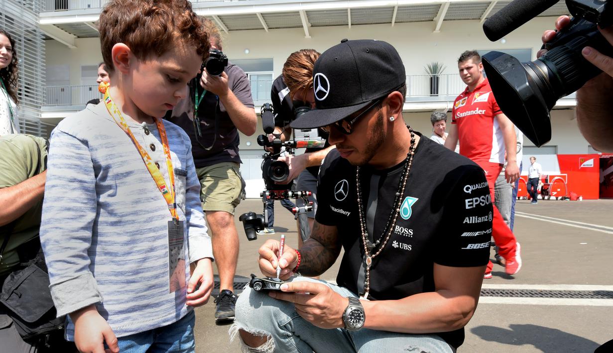 Pebalap Mercedes, Lewis Hamilton memberikan tanda tangan kepada seorang anak di area paddock Sirkuit Autodromo Hermanos Rodriguez, Mexico City, Meksiko, (29/10/2015). (AFP Photo/Alfredo Estrella)
