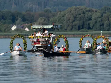 Warga Desa Moos memasuki Pelabuhan Radolfzell sambil manaiki kapal berhias bunga saat mengikuti Pawai Air Mooser di Danau Constance, Jerman, Senin (22/7/2019). Tradisi ini sudah berlangsung selama berabad-abad silam. (Patrick Seeger/DPA/AFP)
