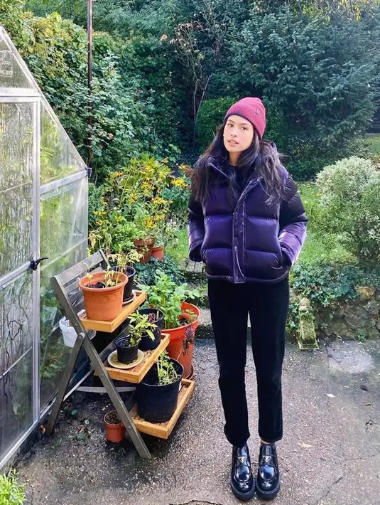 Berpose kece di samping green house milik adik ipar, Tavan Dutton. Maudy Ayunda tampil stylish memadukan jaket puffer ungu, celana hitam, sepatu platform, dan beanie. @maudyayunda.