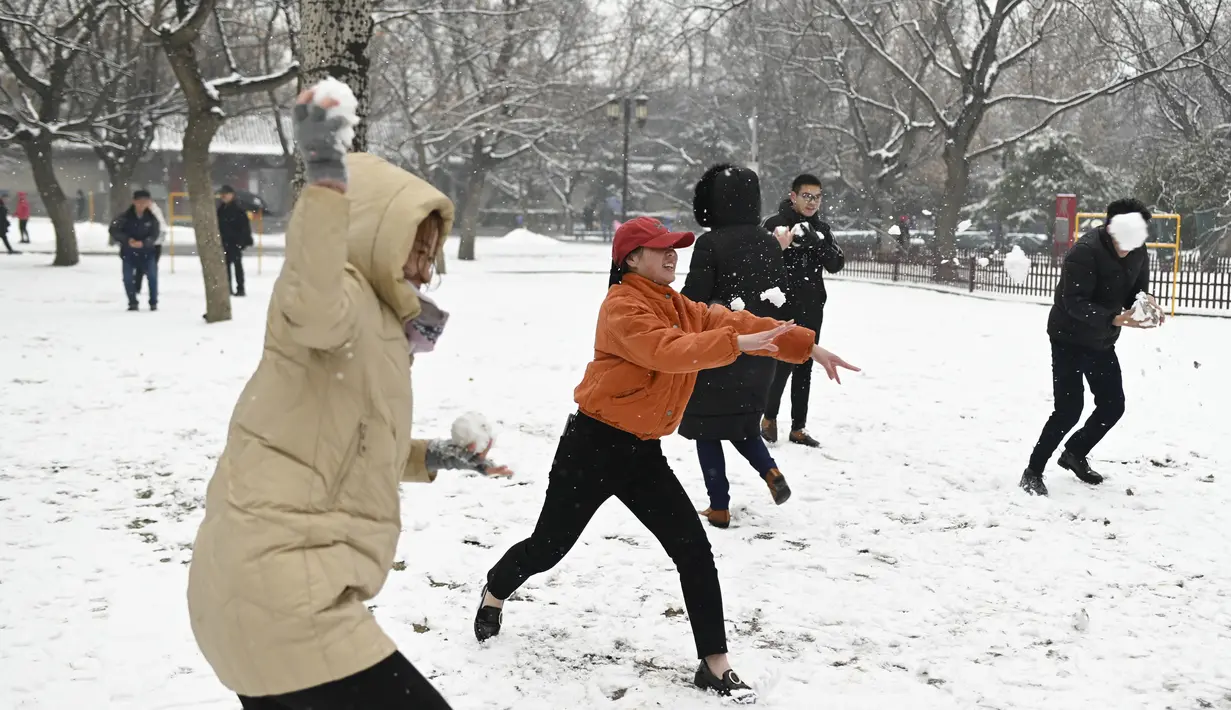 Orang-orang bermain bola salju saat salju turun di sebuah taman di Beijing (16/12/2019). Salju, yang mulai melanda Beijing barat daya sekitar pukul 7 malam. pada hari Minggu, akan mencakup seluruh kota sekitar tengah malam hingga Senin sore, menurut Layanan Meteorologi Beijing. (AFP Photo/Wang Zhao)