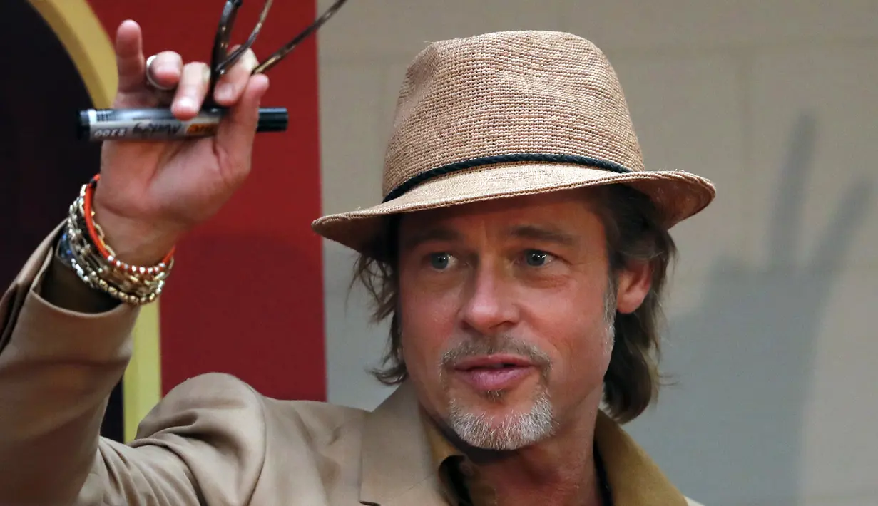 Brad Pitt menyapa penggemar saat menghadiri acara karpet merah untuk film "Once Upon a Time In Hollywood" di Mexico City (12/8/2019). Aktor 55 tahun itu tampil necis dalam setelan jas krem, sepatu boot, dan kemeja mustard. (AP Photo/Marco Ugarte)
