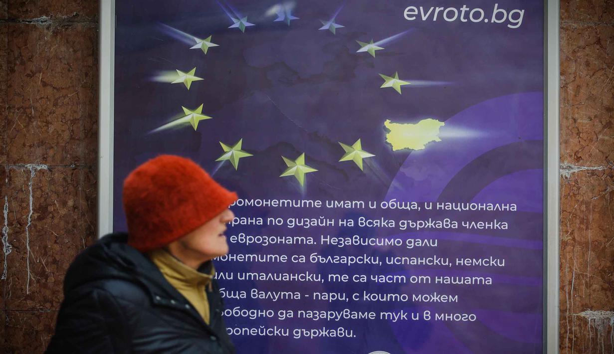 Mengadopsi euro dinilai sebagai fase akhir integrasi Bulgaria ke arus utama Eropa, setelah bergabung dengan NATO, Uni Eropa, kawasan Schengen, dan kini zona mata uang tunggal. Tampak dalam foto, seorang wanita berjalan melewati poster yang menampilkan Bulgaria sebagai anggota Zona Euro ke-21, di Sofia, Kamis 1 Januari 2026, saat negara tersebut bergabung dengan serikat mata uang euro. (AP Photo/Valentina Petrova)
